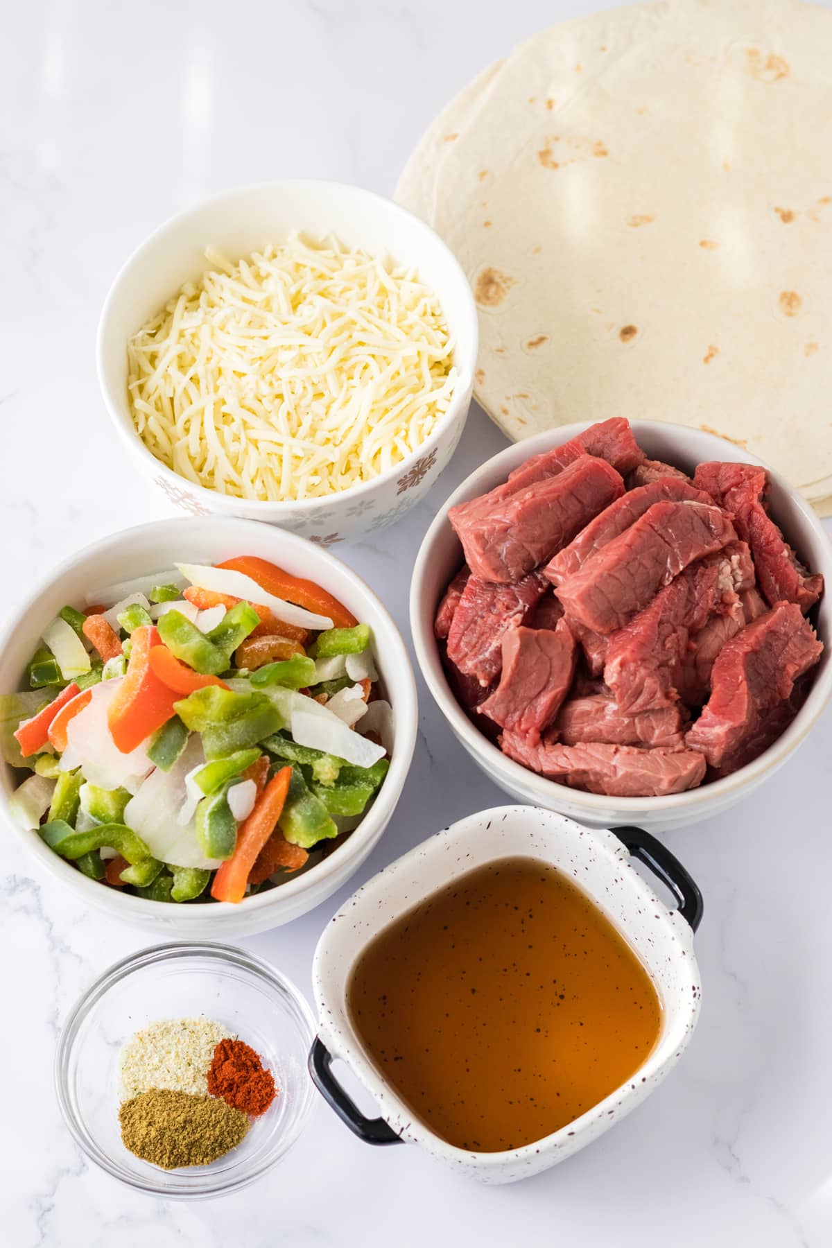Ingredients of Slow Cooker Cheesesteak Quesadillas are the following: Top sirloin steak, cut into strips, Frozen bell peppers and onions, Beef broth, Garlic powder, Onion powder, Smoked paprika, Burrito sized flour tortillas, Shredded mozzarella provolone cheese, Nonstick cooking spray