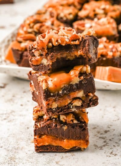 Pile of Turtle Fudge squares with a tray of it on the background.