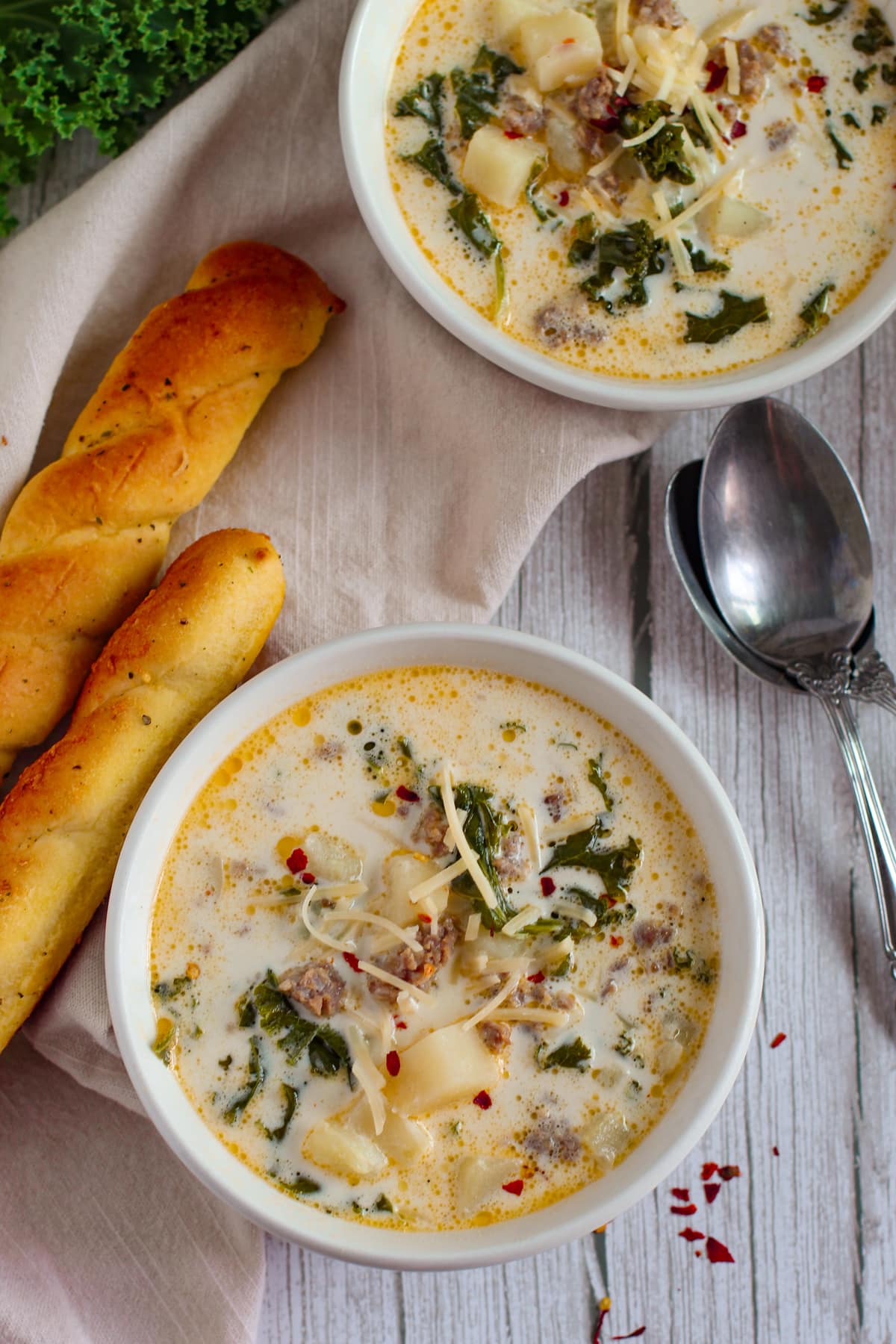 Servings of Olive Garden Zuppa Toscano Soup on a wooden counter with linen and ingredients on the side