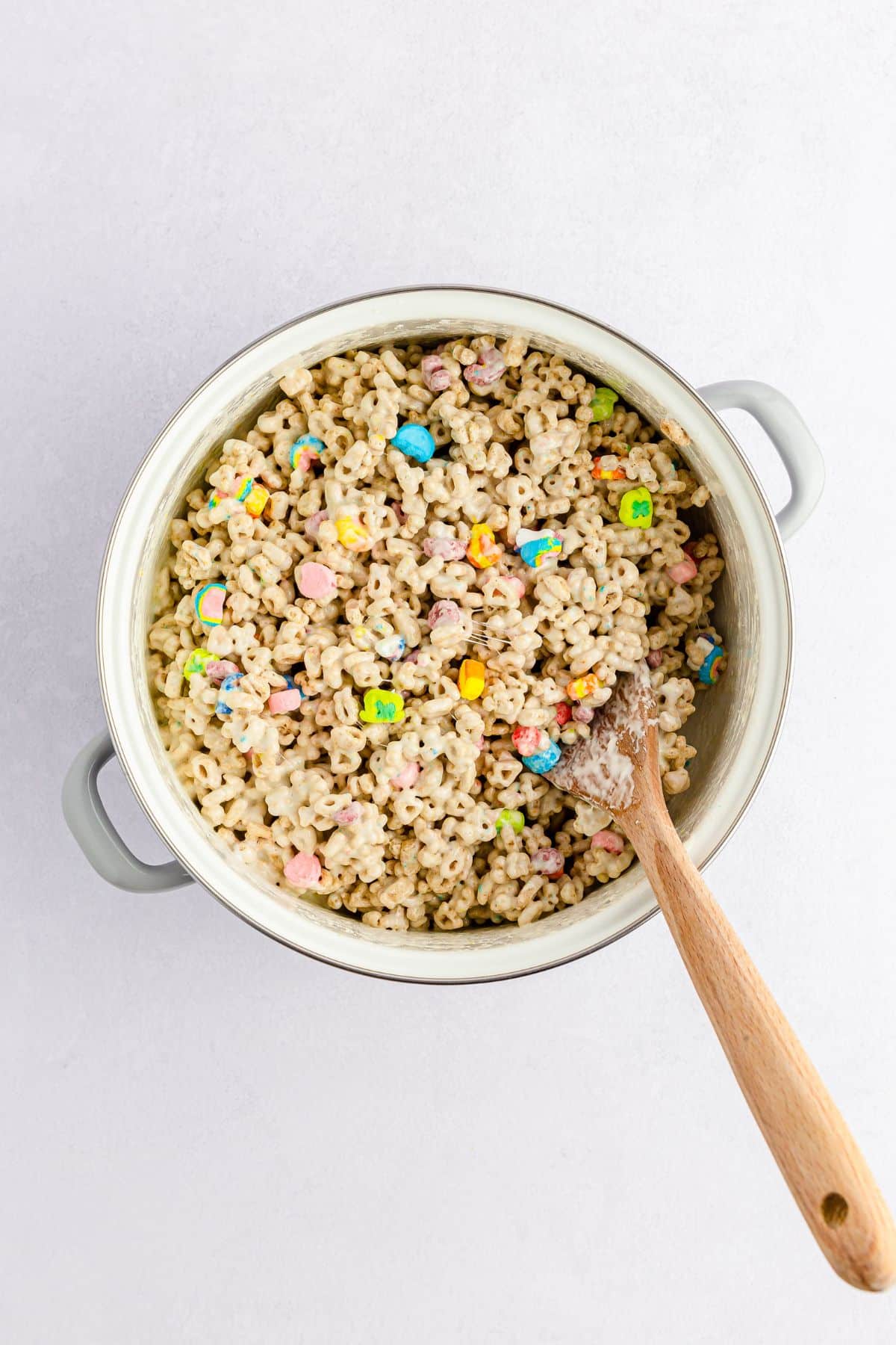 Lucky Charms mixed in with marshmallow mixture and a wooden spoon