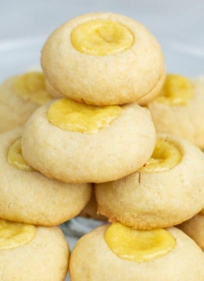 A stack of cheesecake thumbprint cookies on a clear plate.