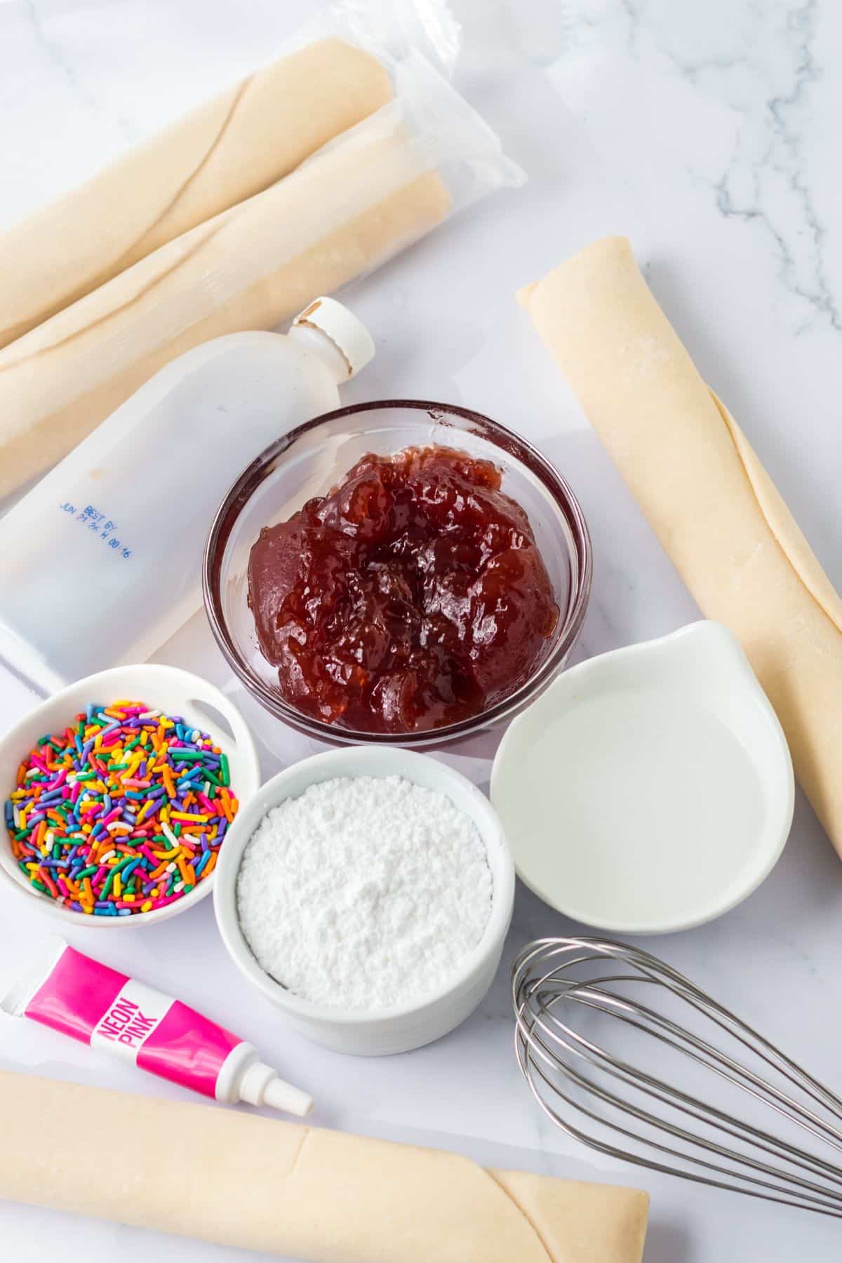 pie crusts, jelly, sprinkles, powdered sugar, and neon pink food coloring on white counter with whisk