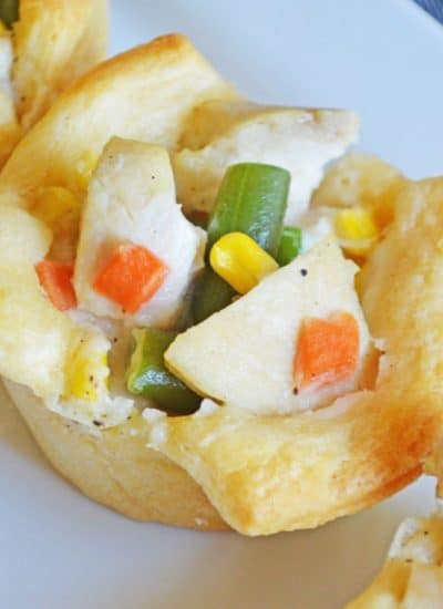Mini chicken pot pies with vegetables and corn in crescent roll cups, served on a white plate.