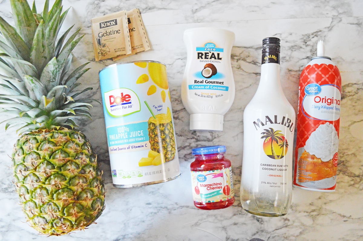 Ingredients for pina colada jello shots include pineapple, pineapple juice, gelatin, whipped cream, coconut rum, cherries, and plastic cups.