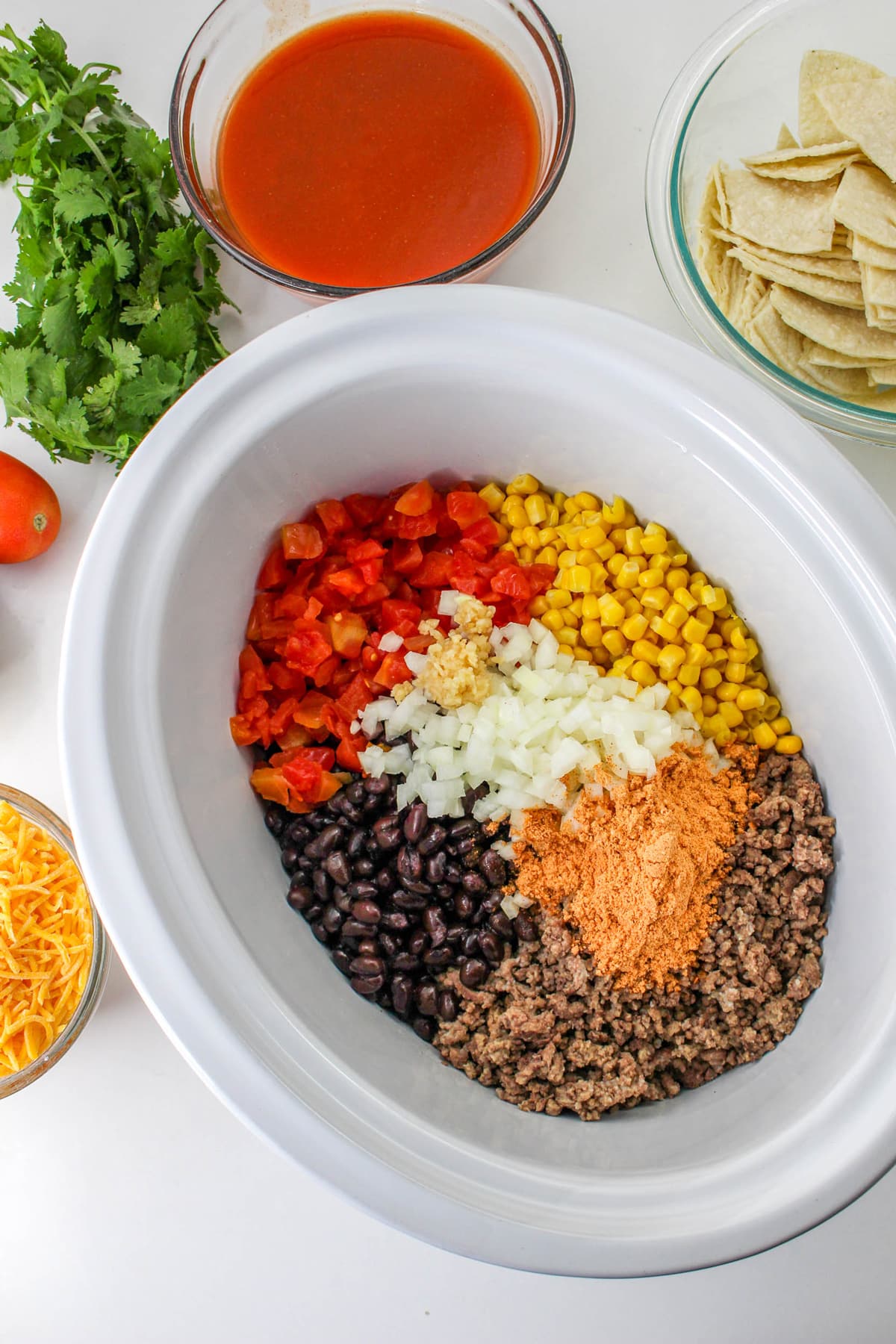 First process in preparing Crockpot Mexican Casserole is to add the ground beef, enchilada sauce, garlic, tomatoes with green chiles, onions, black beans, corn, and taco seasoning to the slow cooker.