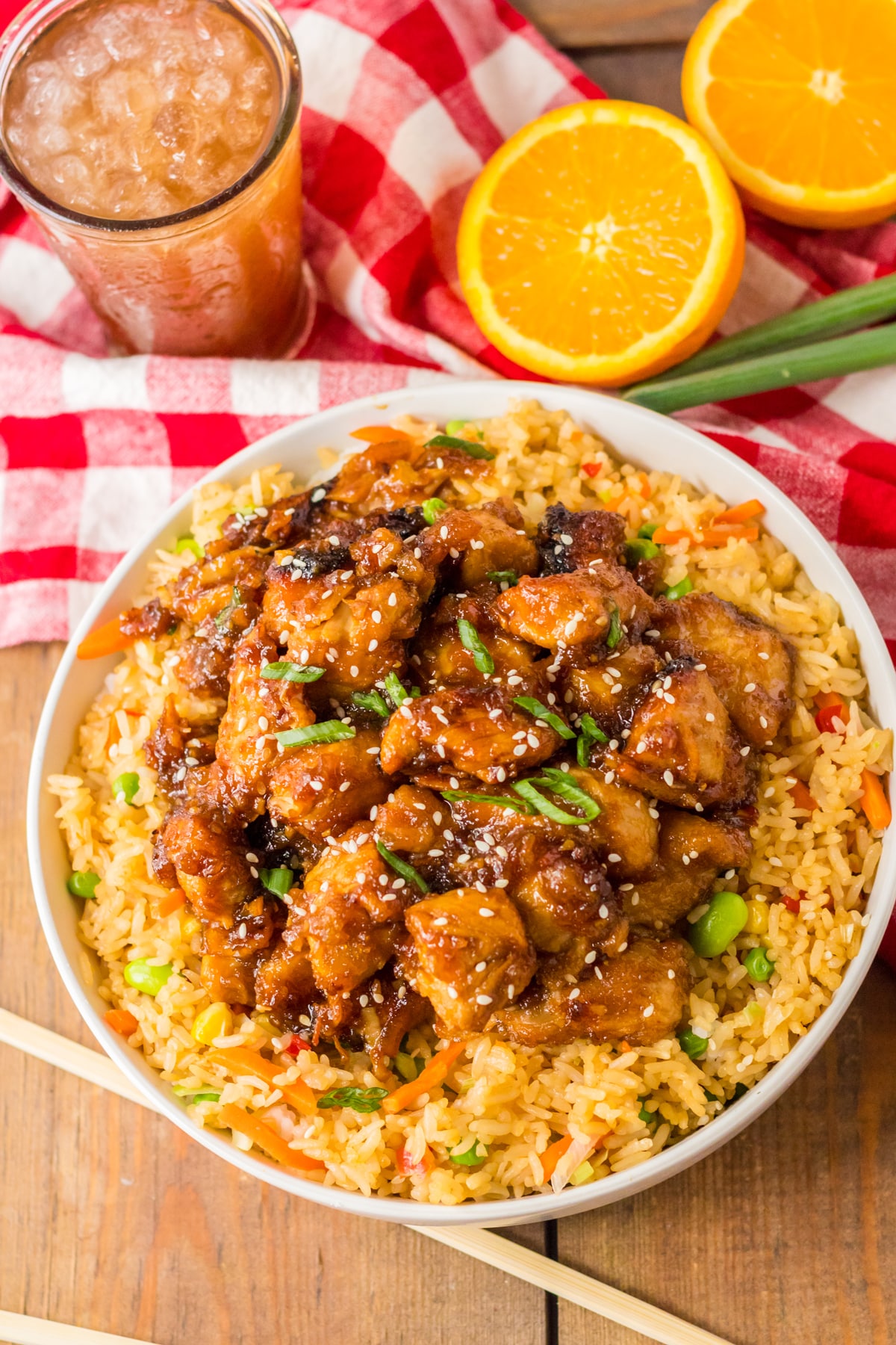 Top view of Slow Cooker Orange Chicken with chopsticks, juice and oranges on a wooden table