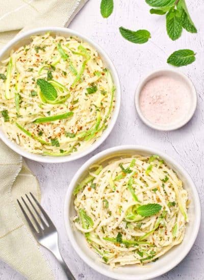two white bowls with zucchini pasta and basil