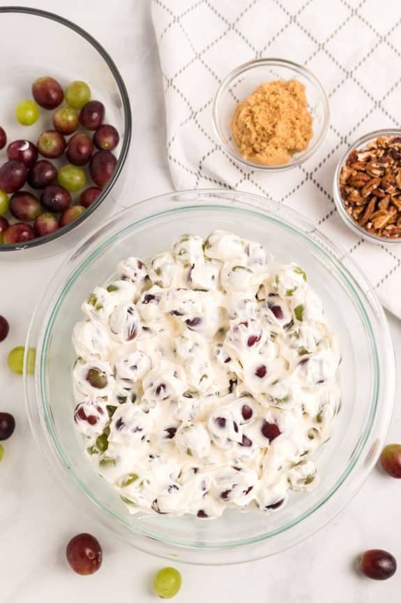 clear mixing bowl with grapes covered in cream cheese mixture
