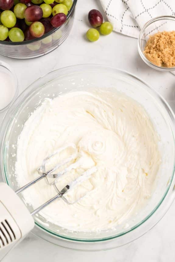 clear mixing bowl with cream cheese mixture with handheld mixer