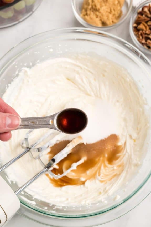 teaspoon with vanilla pouring into cream cheese mixture in mixing bowl