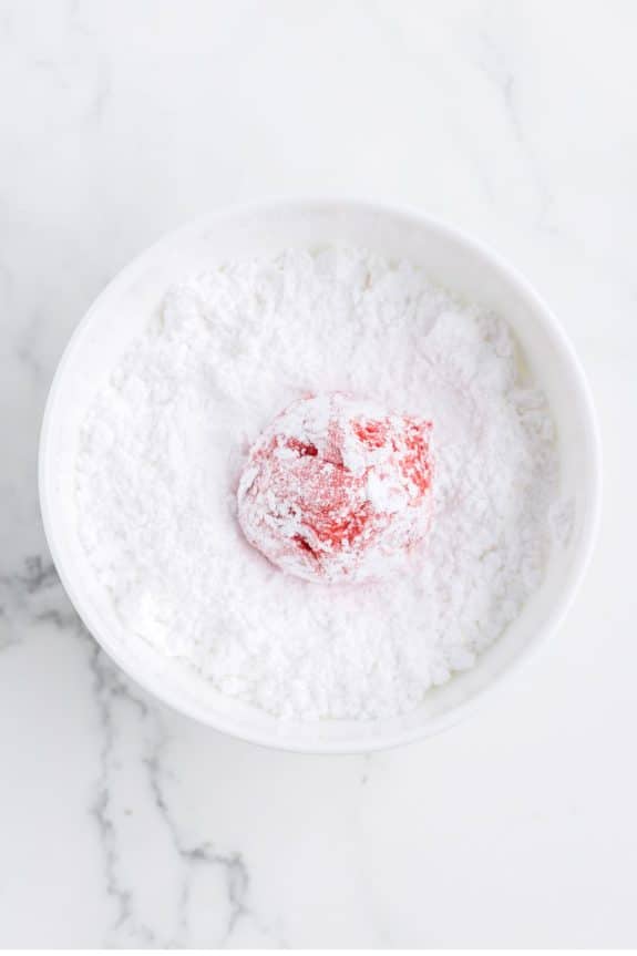 red cookie dough in bowl of powdered sugar