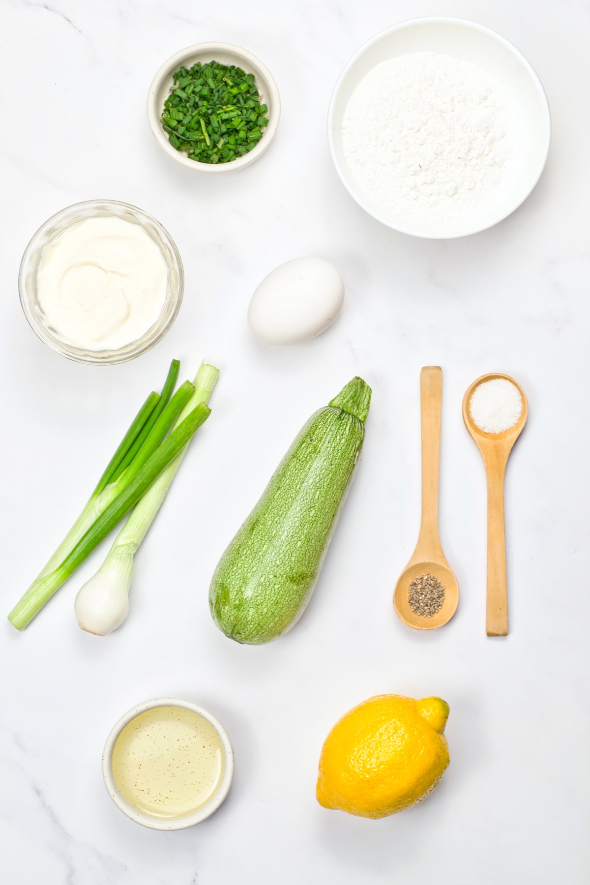 Ingredients for Zucchini Fritters include zucchini, eggs, spring onions, lemon, rice flour, black pepper, salt, chives, vegetable oil, and vegan sour cream