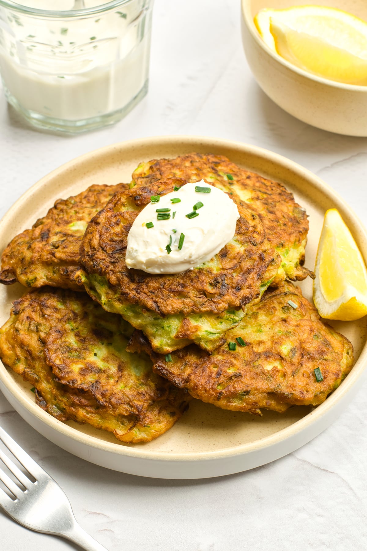 Zucchini Fritters on a serving plate with utensils on the side.