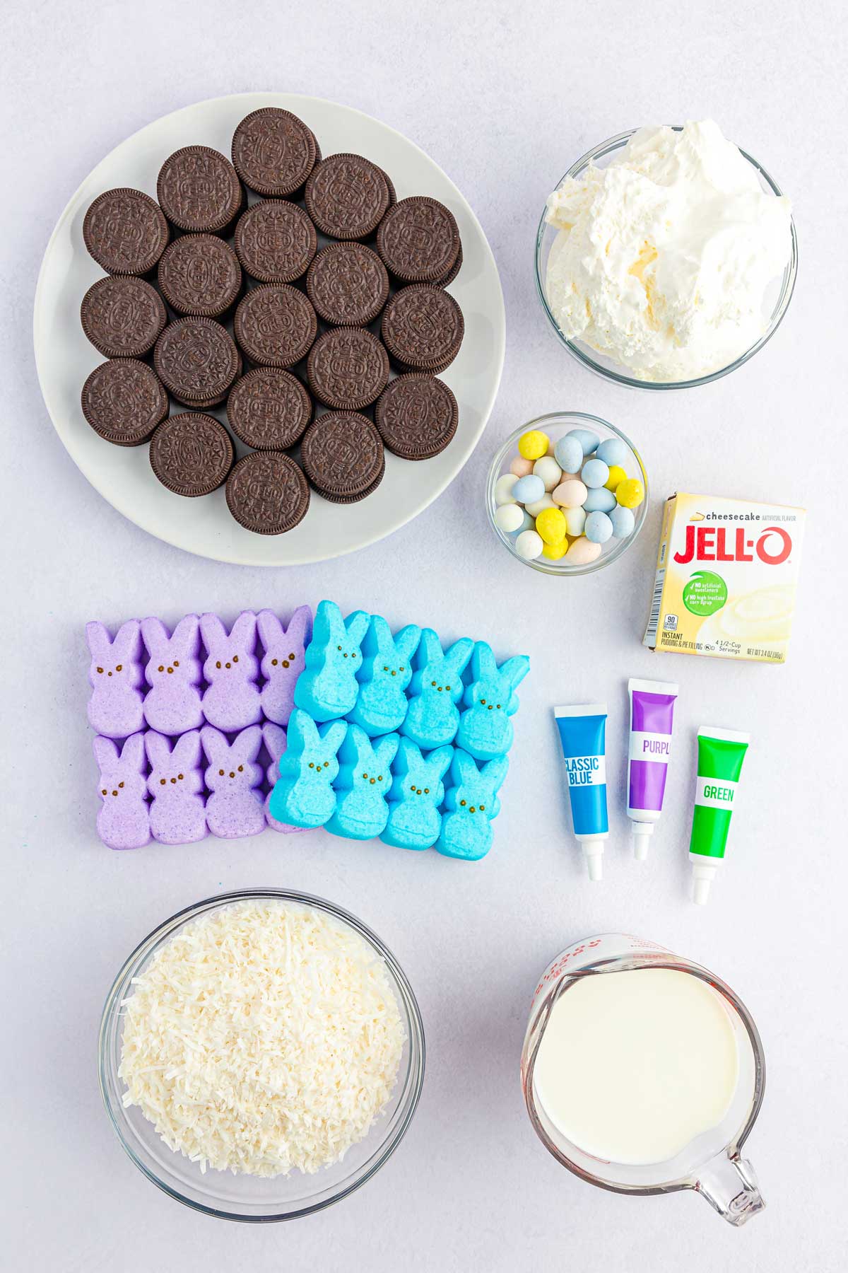 Easter dirt cups ingredients are the following: oreo cookies, cheesecake or white chocolate instant pudding mix, cold milk, cool Whip, thawed, gel food coloring in choice of colors, coconut shreds, cadbury mini eggs and peeps marshmallow bunnies
