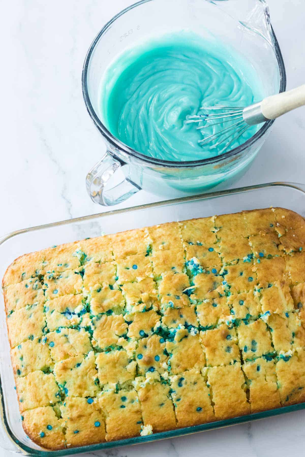 yellow sheet cake cut in cubes with teal frosting in measuring cup
