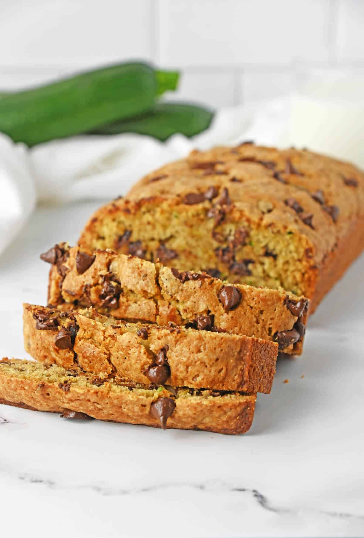 chocolate chip zucchini bread sliced on white counter with glass of milk