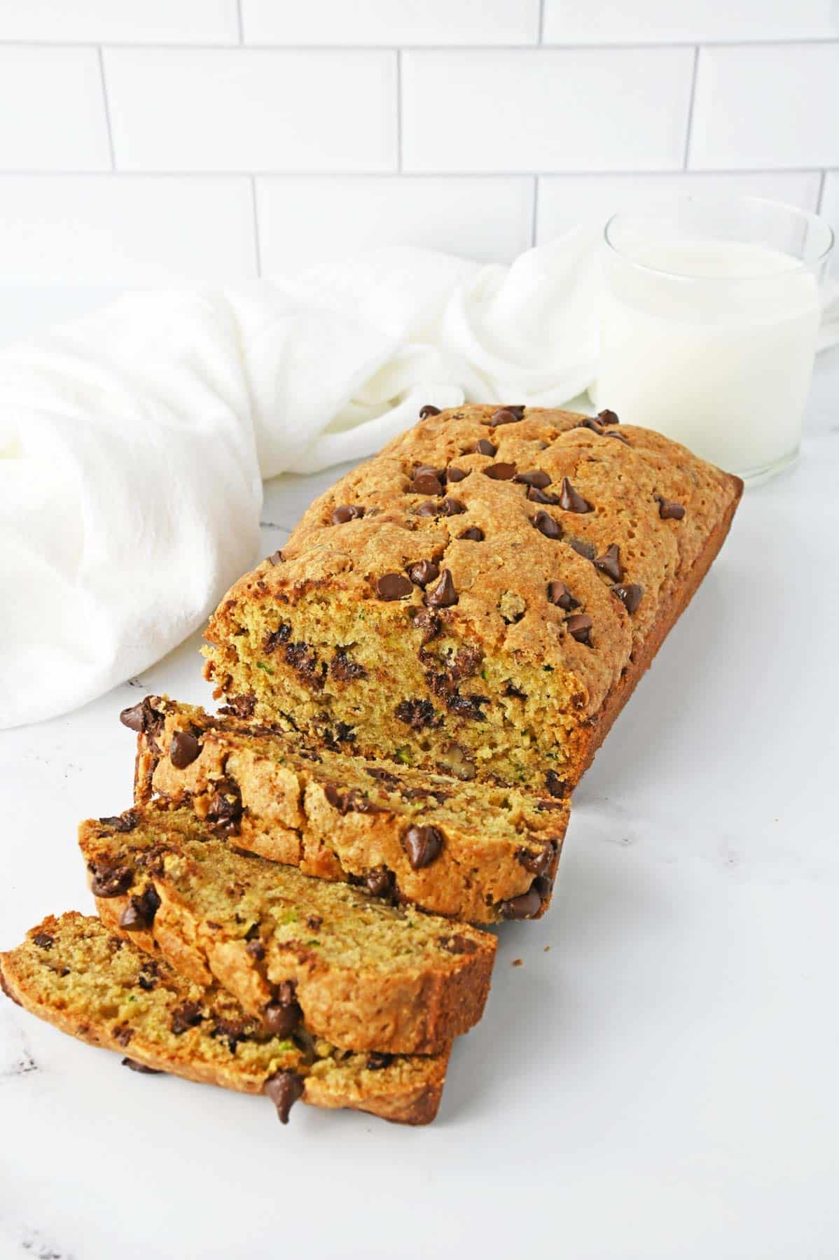 chocolate chip zucchini bread sliced on white counter with glass of milk