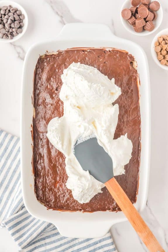 chocolate pudding layer with whipped cream later and spatula spreading it out
