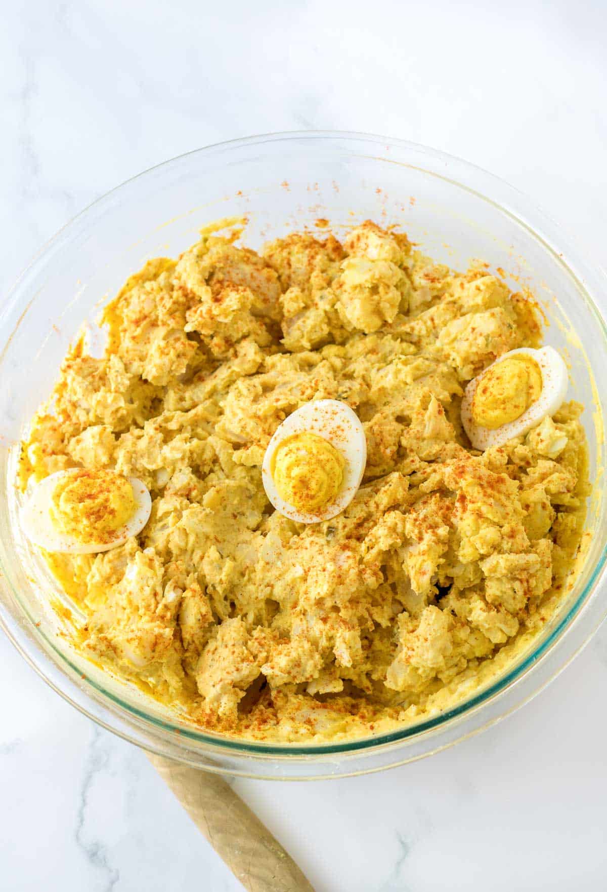 clear mixing bowl with deviled eggs on top of potato salad