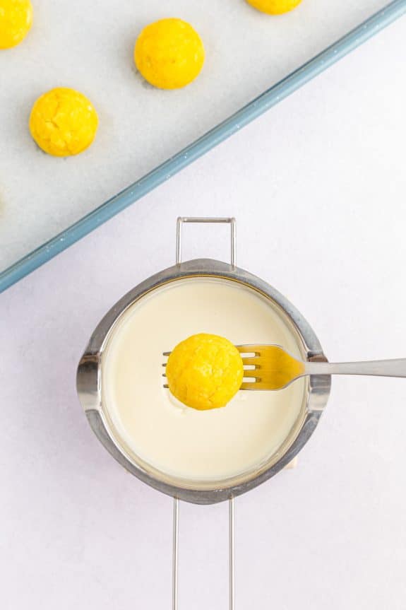 yellow cake ball on fork above saucepan with melted white chocolate