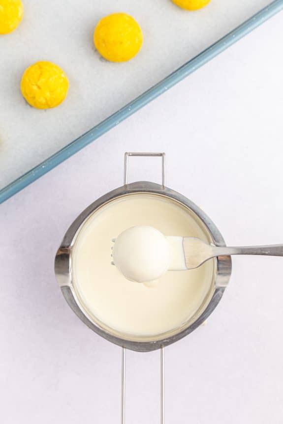 fork dipping yellow cake ball in white chocolate in saucepan