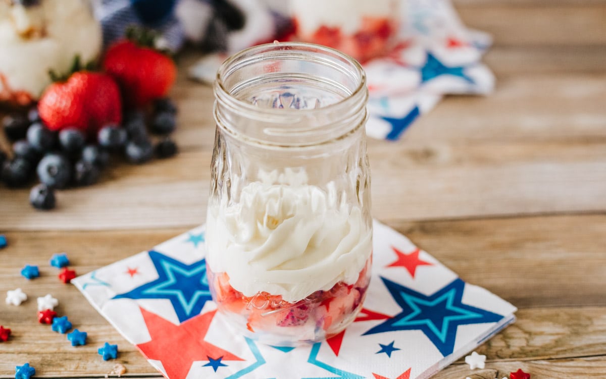 thin mason jar with chopped strawberries and whipped cream layers