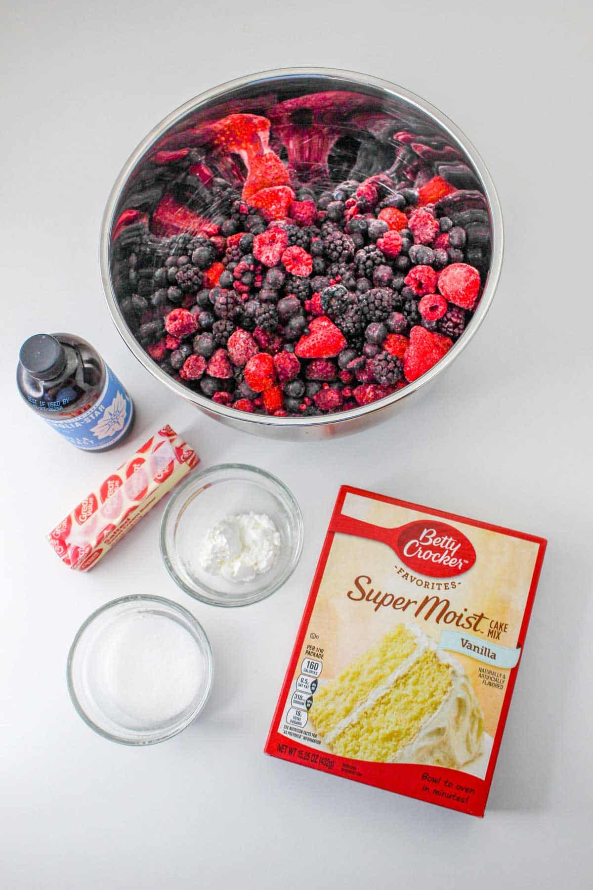 blackberries, raspberries and small strawberries in bowl, vanilla, butter, sugar and vanilla cake mix on counter