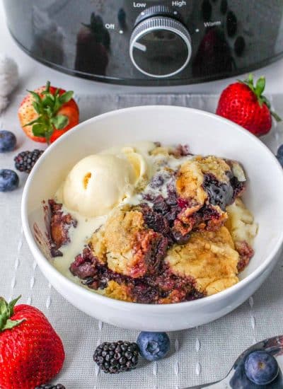 berry cobbler with ice cream in bowl next to slow cooker