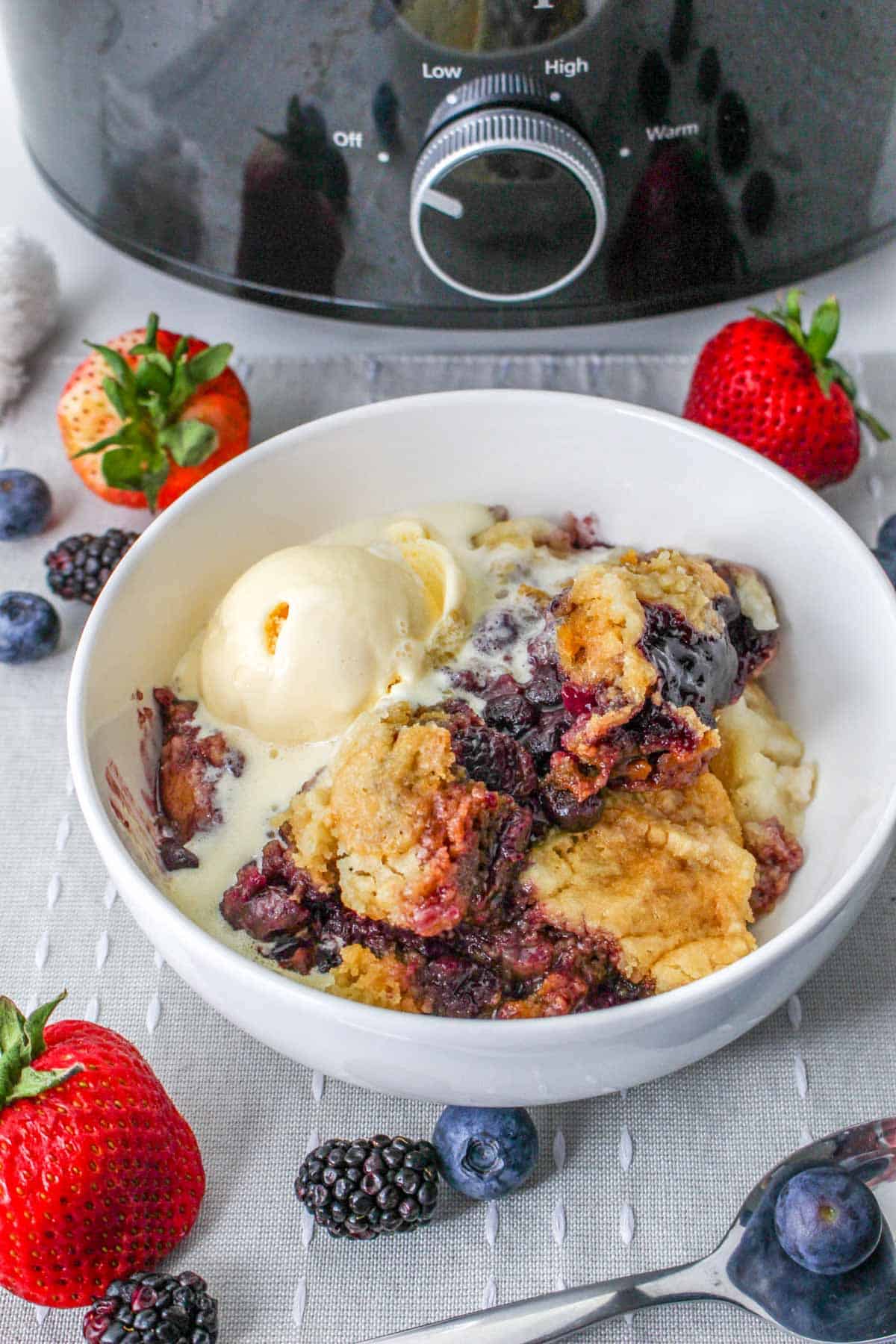 berry cobbler with ice cream in bowl next to slow cooker - crockpot cobbler with cake mix