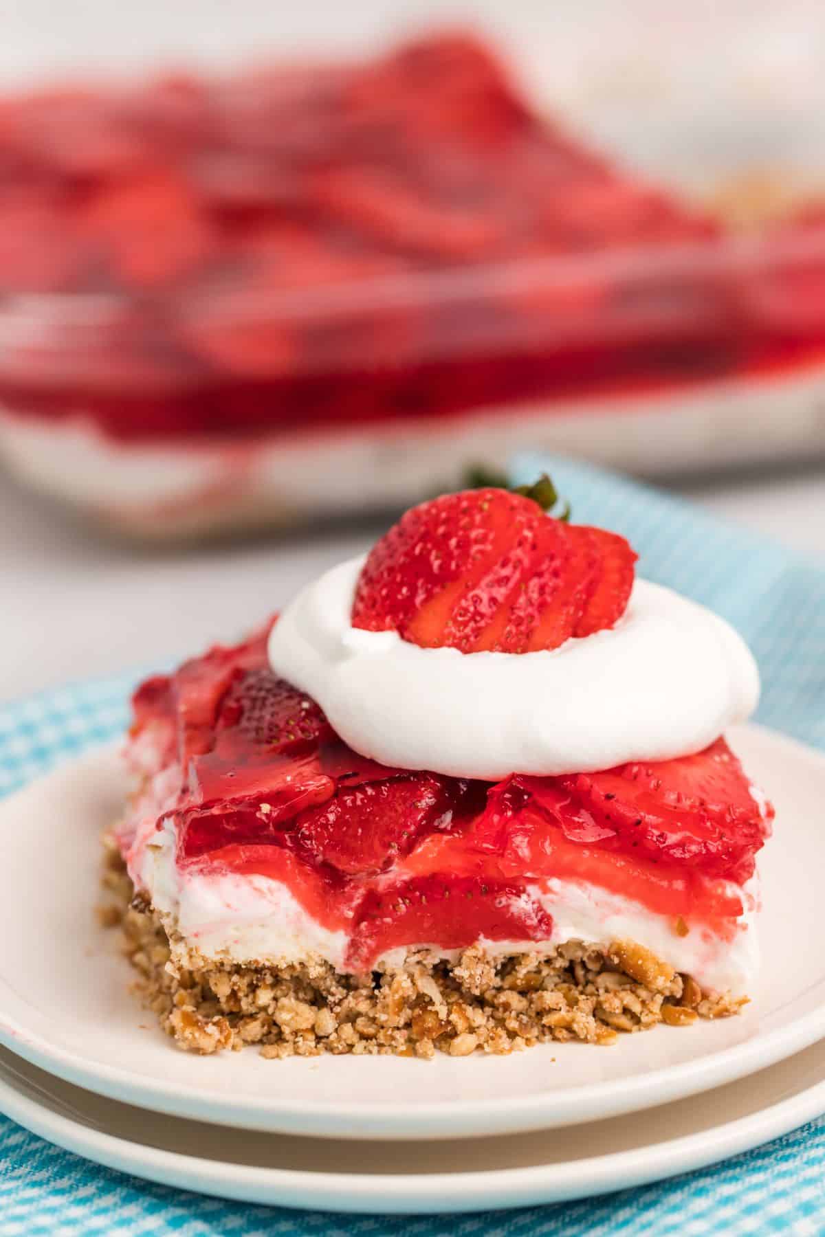 slice of strawberry pretzel salad with whipped cream and a sliced strawberry on top