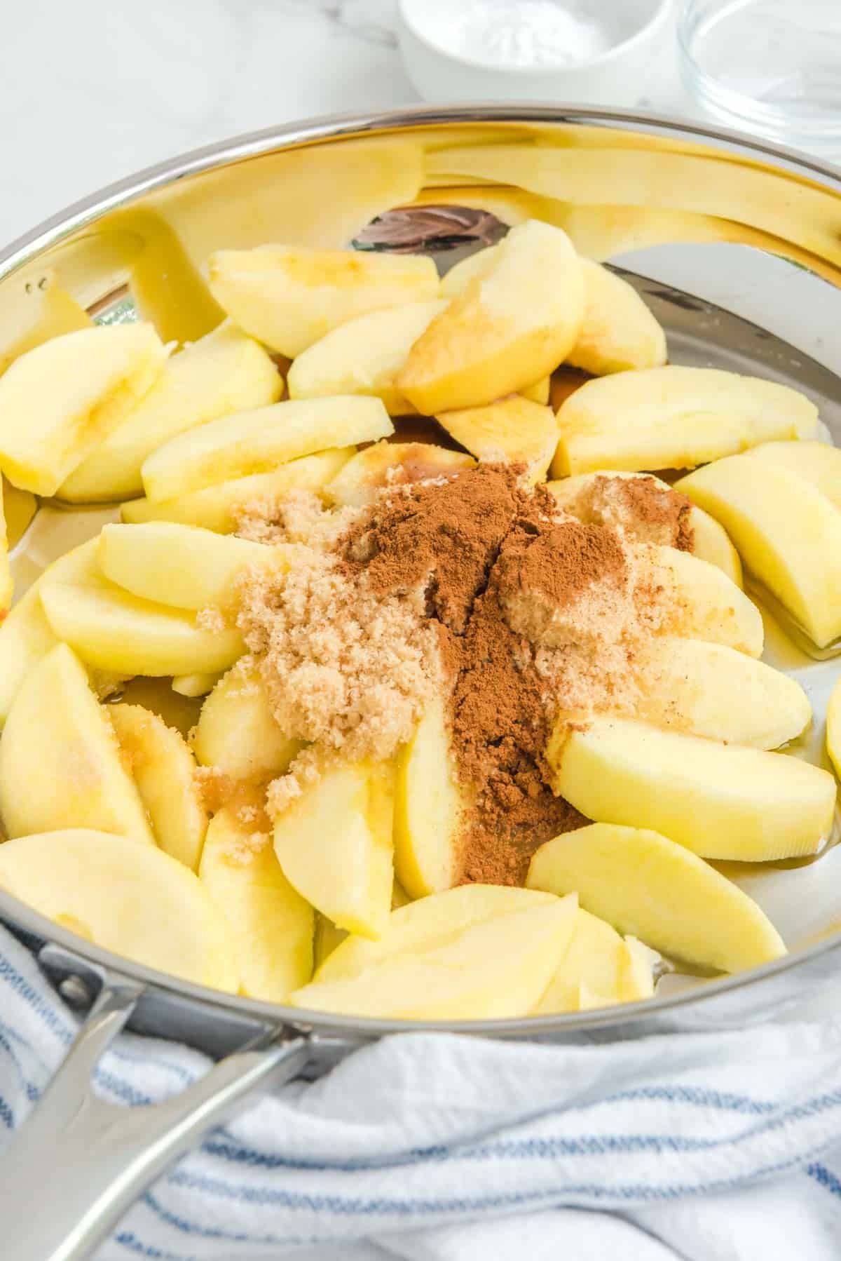 raw sliced apples with cinnamon and brown sugar in saucepan
