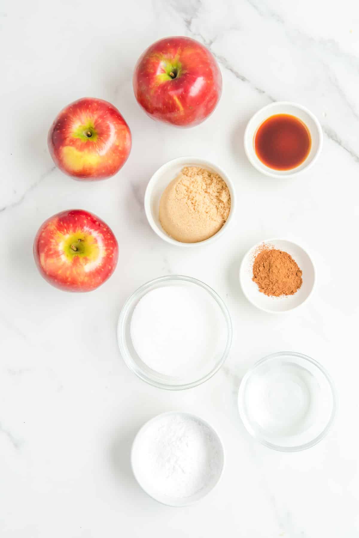 three red apples, and spices in bowls on counter