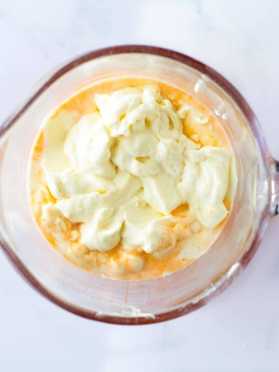orange mixture with cream cheese mixture in glass measuring cup