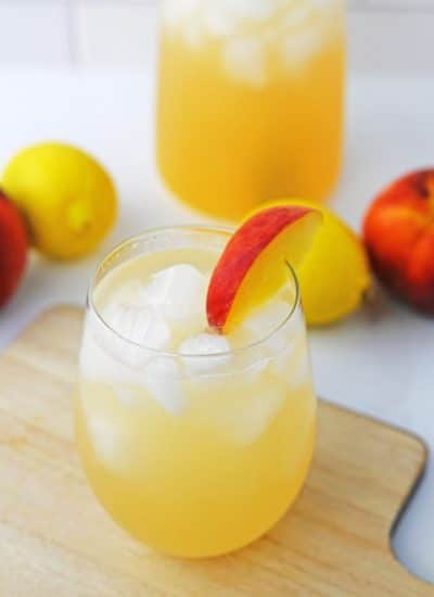 peach lemonade with ice in stemless glass with slice of a peach on the side