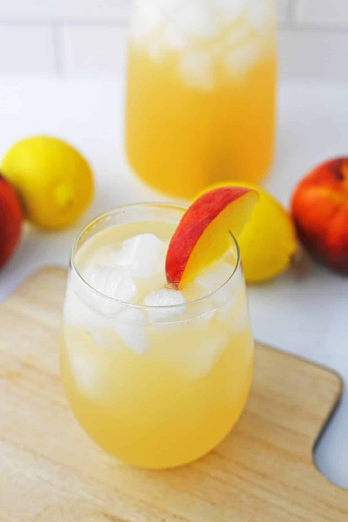 peach lemonade with ice in stemless glass with slice of a peach on the side