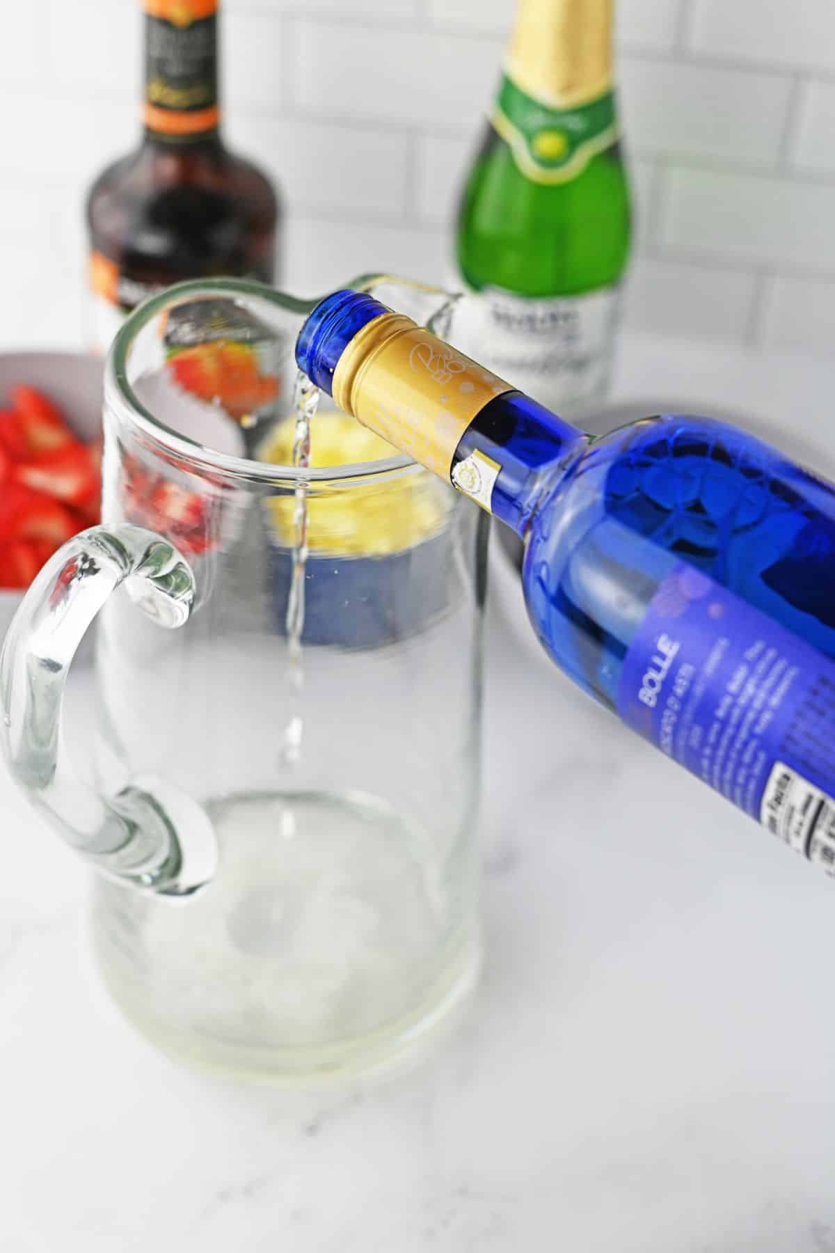 blue bottle of Moscato being poured into large glass pitcher