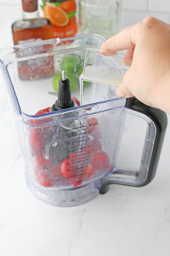 liquor being poured into blender with strawberries
