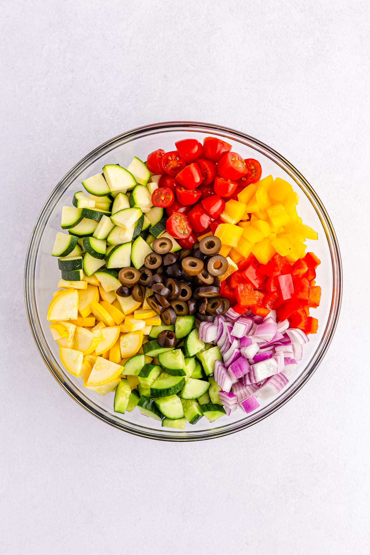 Mixing all ingredients for California Spaghetti Salad include spaghetti, cherry or grape tomatoes, English cucumber, red bell pepper, yellow bell pepper, red onion, black olives, yellow squash diced, and Zucchini