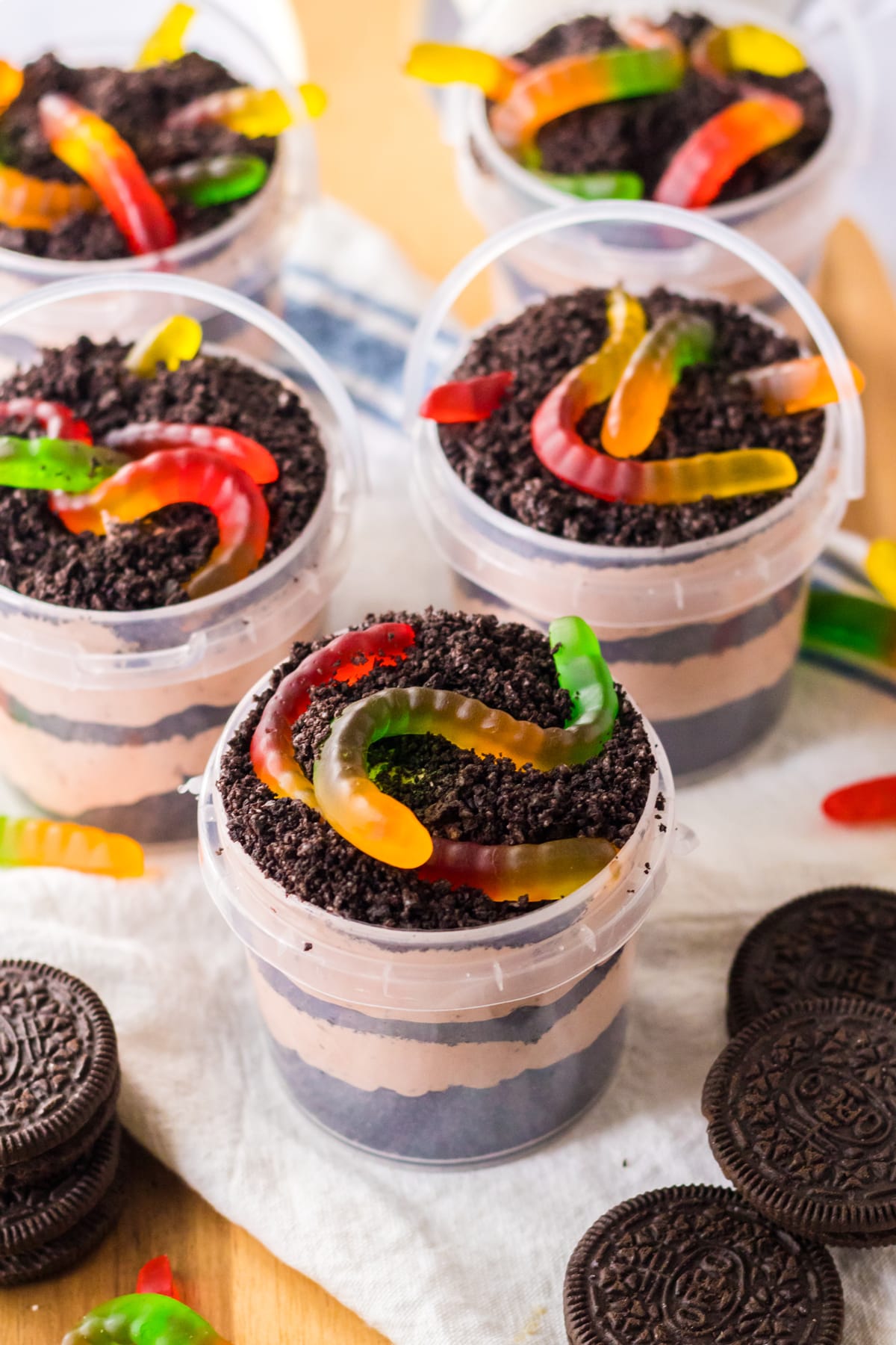 Servings of Dirt Cake Pudding Buckets with oreos and gummies on a white table cloth.