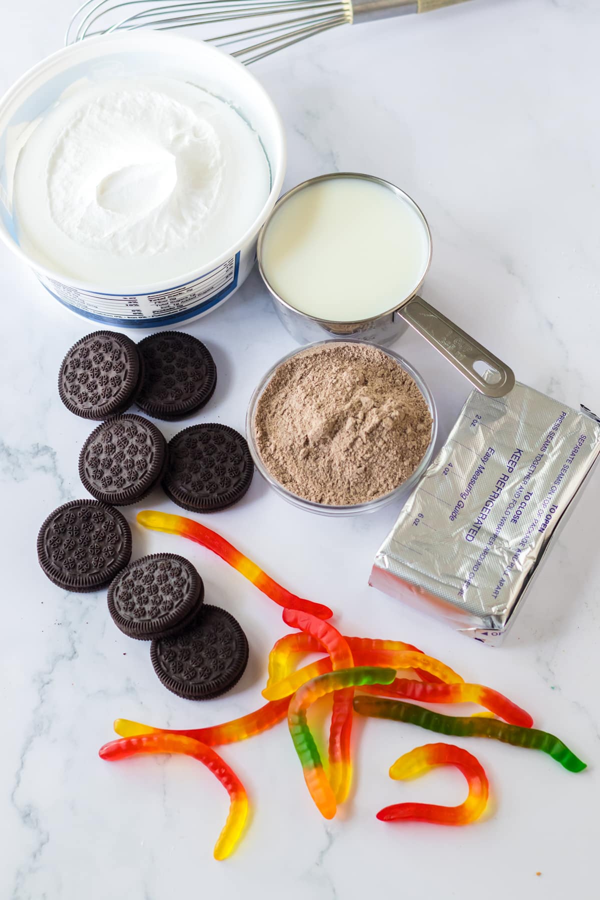 Ingredients for Dirt Cake Pudding Buckets on a white counter. It includes instant chocolate pudding mix, cream cheese, softened, milk, whipped topping, oreos, crushed, gummy worms and clear buckets (8 oz)
