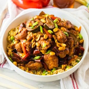 Recipe thumbnail for Slow Cooker Kung Pao Chicken on a white bowl with linen and chopsticks