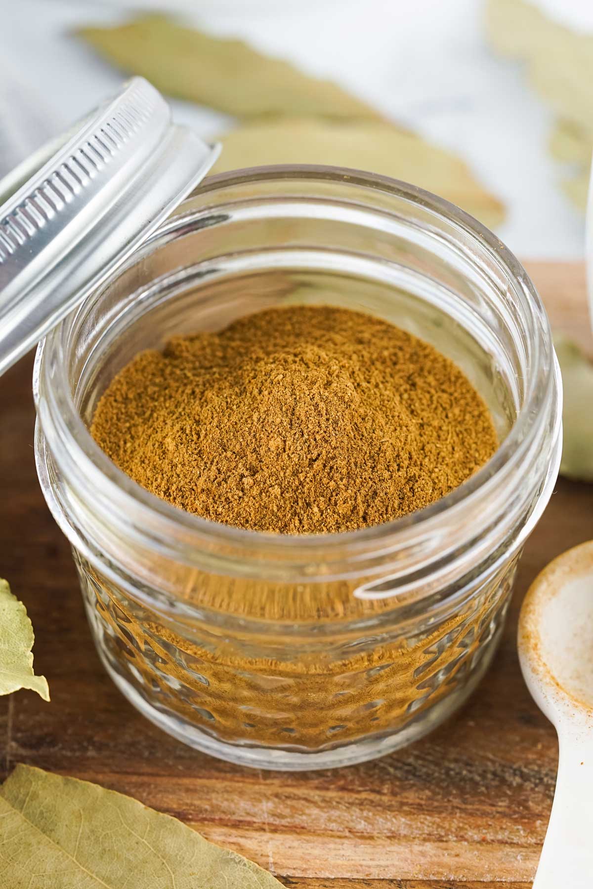 A small jar of Pumpkin Pie Spice with bay leaf on a wooden table