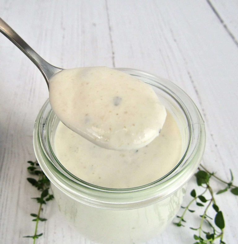 A spoonful of dressing in a jar on a white table.