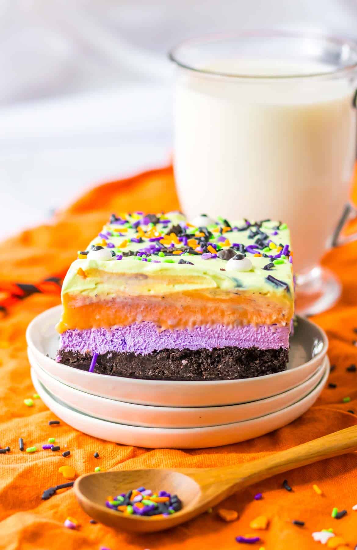A plate of purple, orange and green cake with a spoon and a glass of milk.