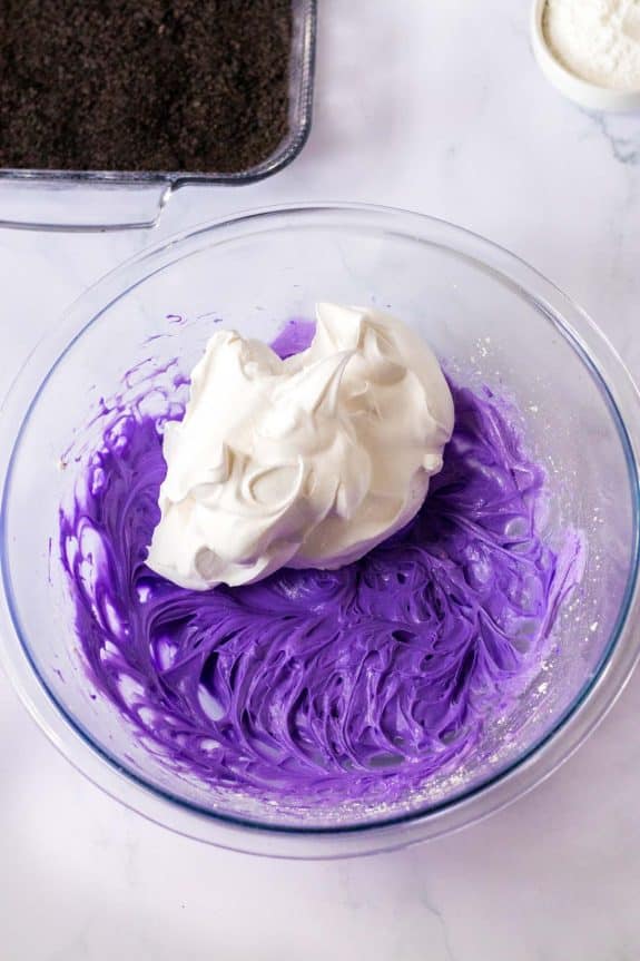 A bowl of purple icing with whipped cream in it.