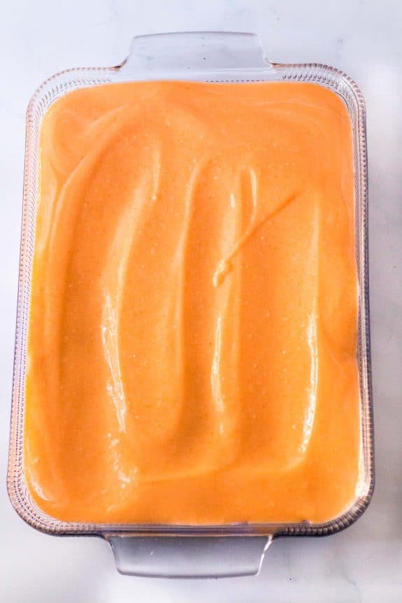 A bowl of orange icing in a clear dish.
