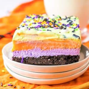 A slice of rainbow cheesecake on a plate with a cup of coffee, perfect for Halloween indulgence.
