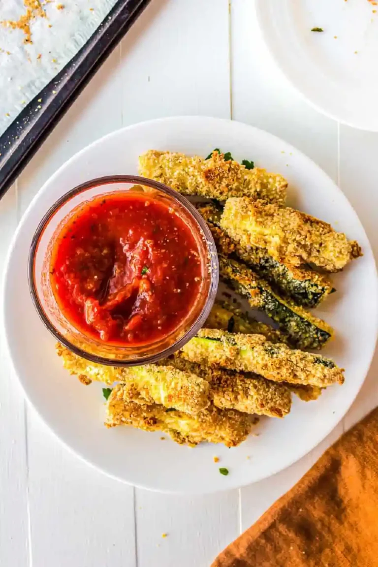 Fried zucchini sticks on a plate with dipping sauce.