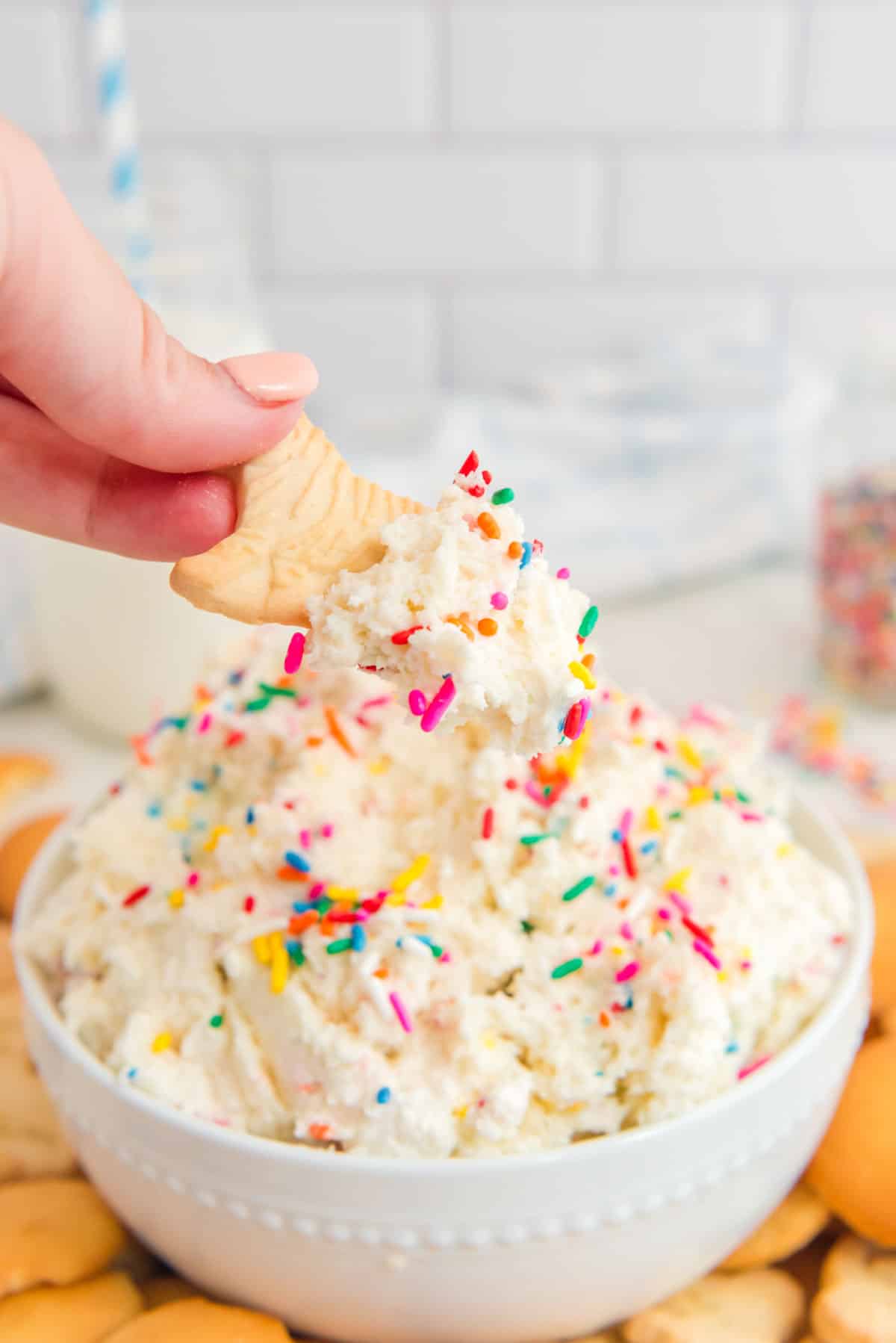 A person dipping a cracker into a bowl of dip with sprinkles.