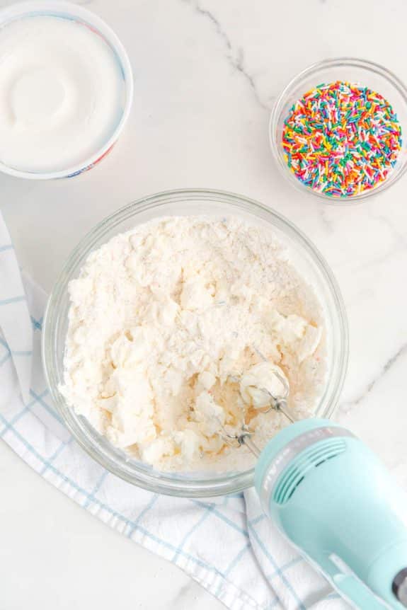 A bowl of icing with icing sugar and sprinkles.